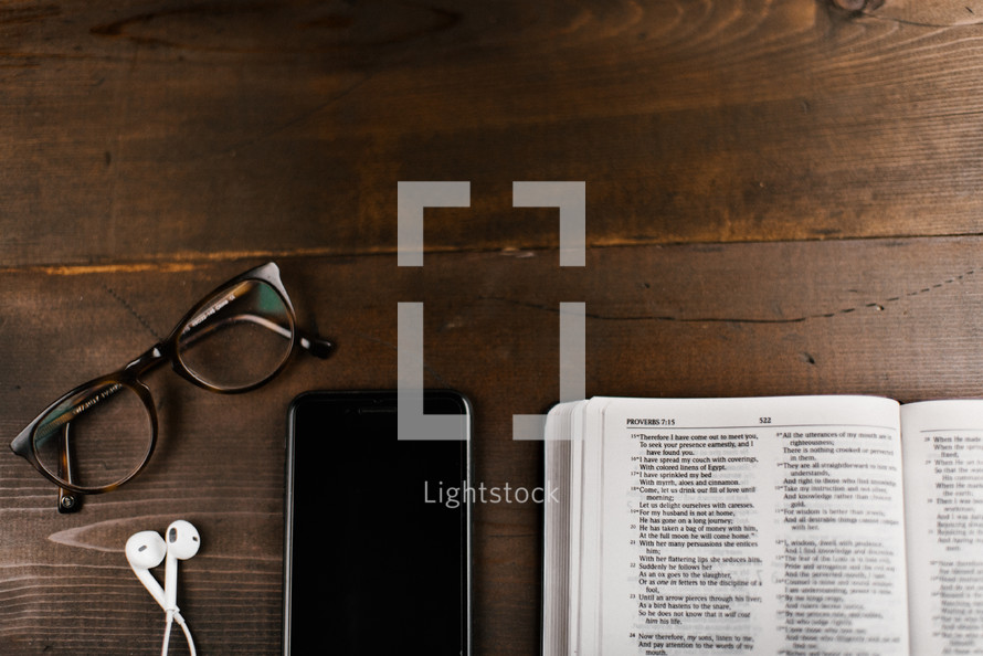 reading glasses, iPhone with earbuds, and open Bible 