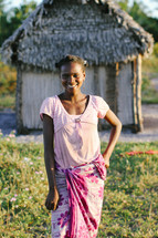 young woman standing in front of a hut 