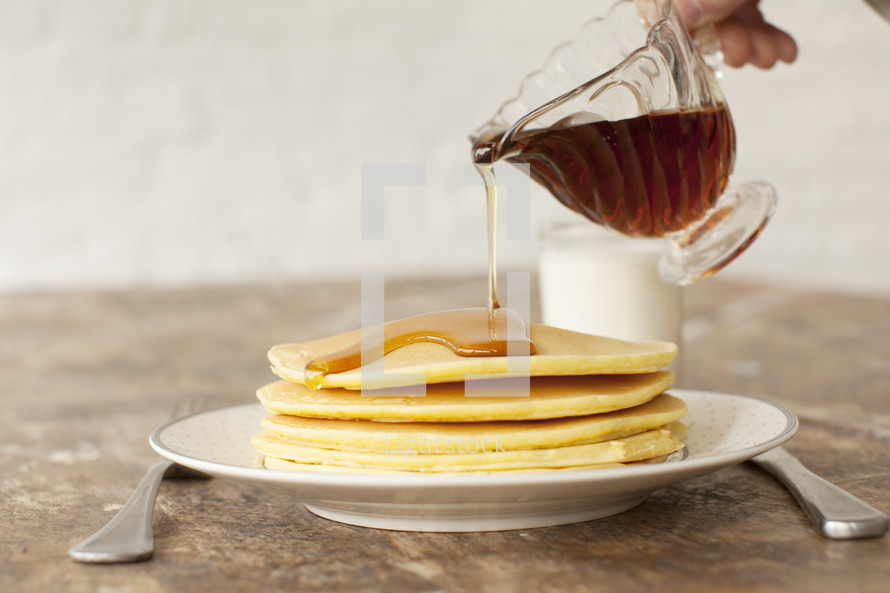 Pouring syrup on a stack of pancakes.