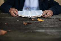teen boy reading a Bible at a picnic table 