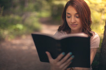 woman sitting outdoors reading a Bible 