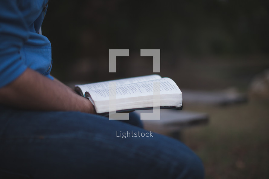 Holding an open Bible outside.