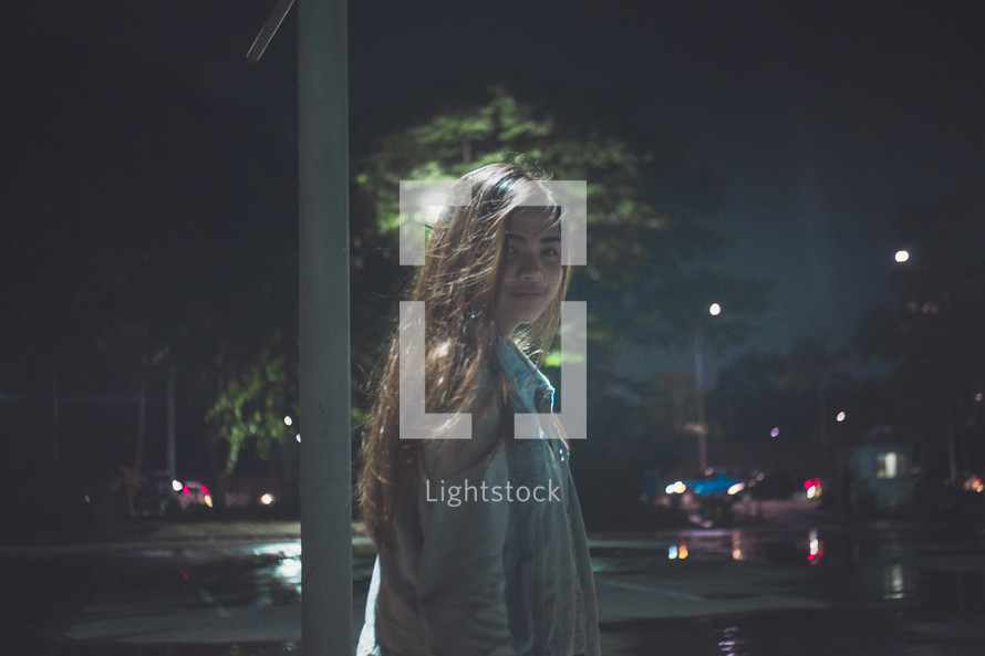 a girl standing in a parking lot at night 