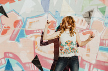 a joyous playful woman standing in front of a graffiti covered wall 