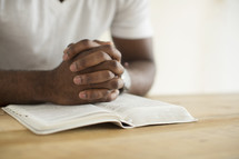 a man with praying hands over the pages of a Bible. 