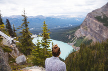 A woman sitting on a mountaintop looking out at the view 