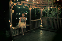 Woman sitting in a lighted gazebo at night.