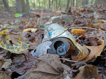 Old metal drink can abandoned in leaves in forest as litter