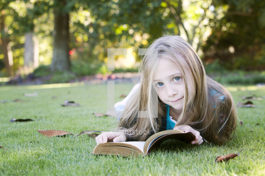Child reading the Bible in the grass outdoors