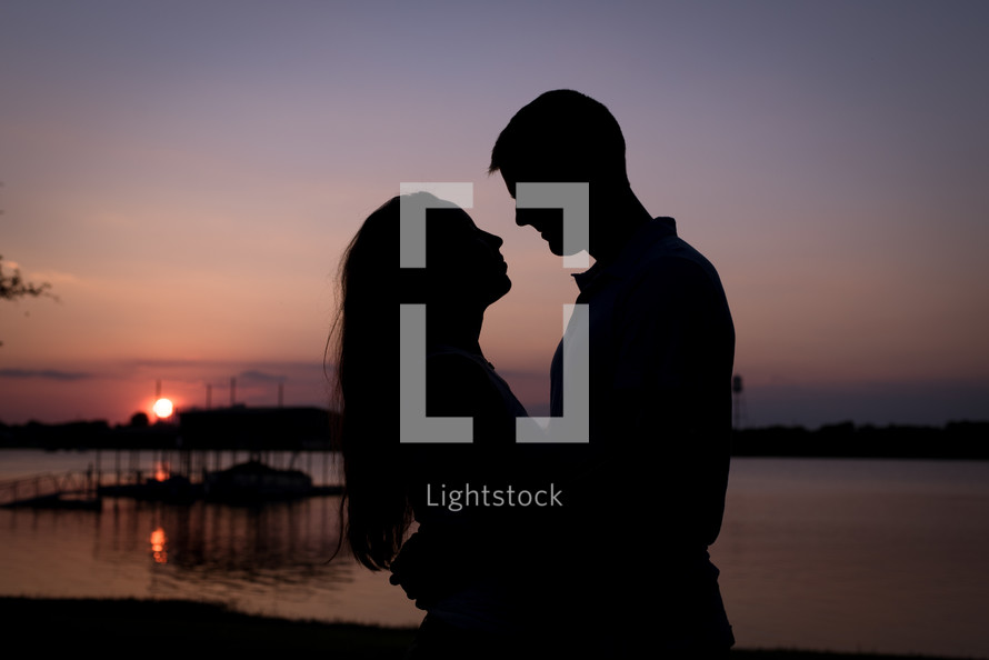 silhouette of a couple in love standing by a lake at dusk 
