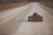 a gravel road with suitcase and hat