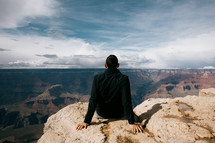 man sitting at the edge of a canyon landscape 