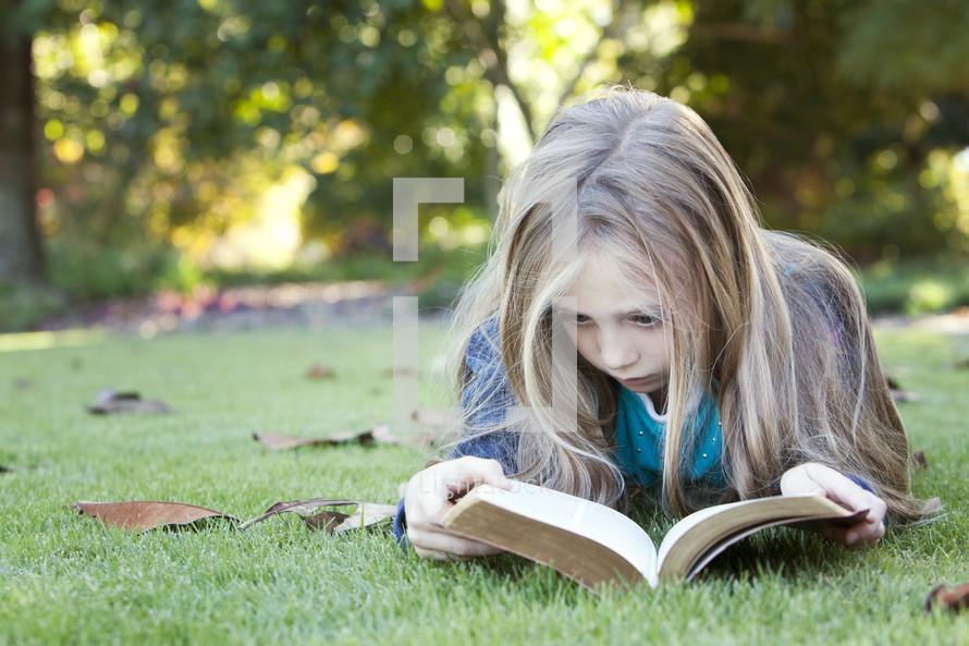 Young girl child reading the Bible outdoors in a park