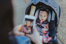 a mother taking a picture of her baby daughter in a stroller 