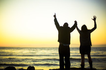 couple with raised arms on a beach - worship to God