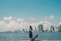a girl holding an umbrella looking across a bay at a city 