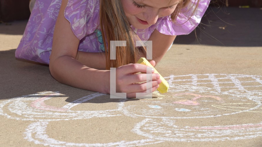 A little girl drawing an Easter bunny with sidewalk chalk 