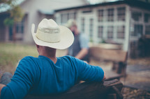 a man in a cowboy hat sitting on benches in a background 