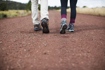 Legs and feet of a man and woman walking down a country road.