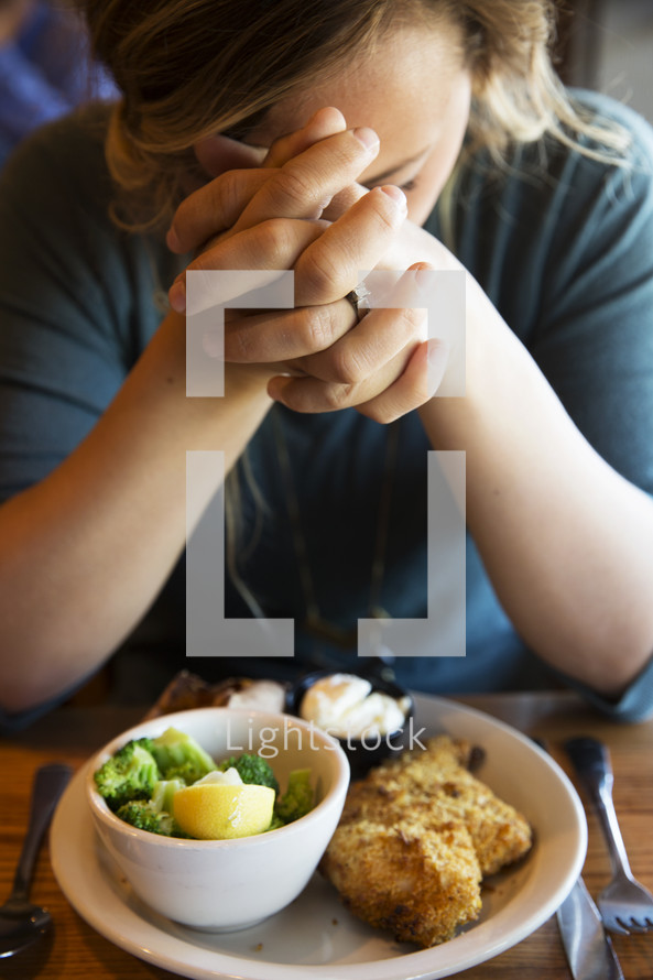 woman with praying hands over a plate at dinner 