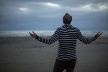 man with outstretched arms standing on a beach 