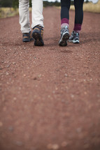 The legs and feet of a man and woman walking down a country road.