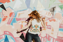 A young woman dancing in front of a colorful painted wall.