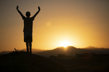 teen boy standing in warm sunlight with arms raised