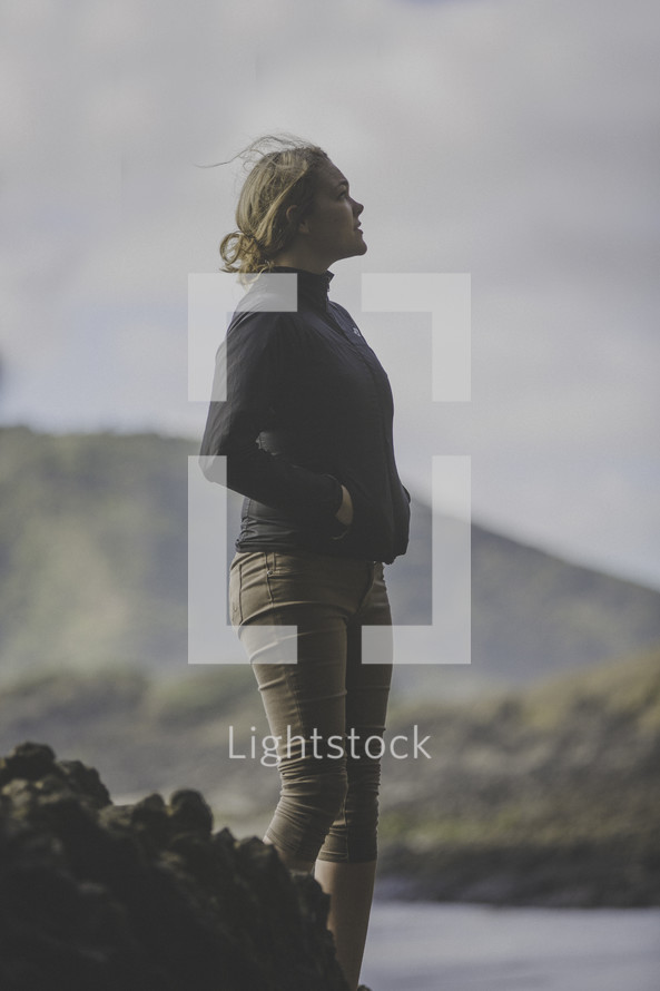 a woman standing alone outdoors on a rocky terrain 