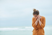 a woman standing on a beach praying 