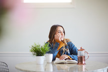 a woman reading a Bible sitting at a kitchen table and staring off in thought 