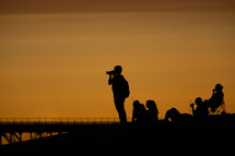 silhouettes of people taking pictures of a sunset on a beach 