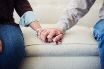 mature couple holding hands on a couch.