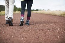 The legs and feet of a man and woman walking down a country road.