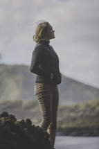 a woman standing alone outdoors on a rocky terrain 
