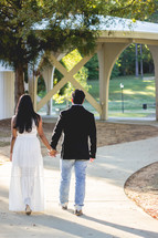 a couple walking holding hands on a sidewalk 