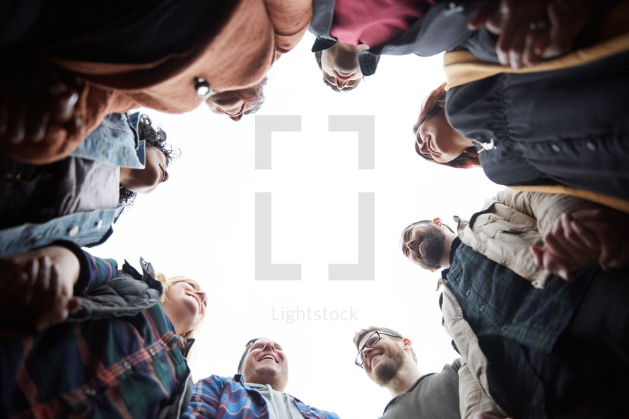 looking up into a group prayer circle with men and women holding hands in prayer in fall 