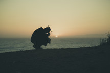 silhouette of a graduate kneeling in prayer on a beach
