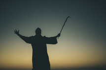 silhouette of a man in a robe with a staff raised to the sky