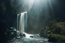 A beautiful waterfall and stream with lights shining down.