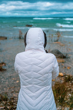 a woman in a coat looking out at the ocean 