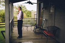 man buttoning a shirt on a porch 