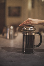 A hand pressing down on a French Press