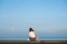 young woman sitting on a concrete wall by the ocean 