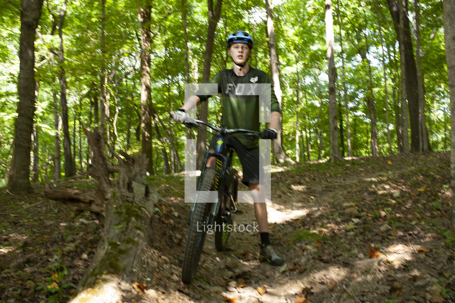 a teen boy riding a bicycle in a forest 