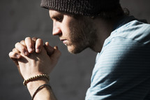 a man with a wool cap and praying hands 