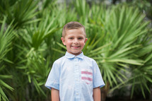 smiling boy child standing in front of palm trees 