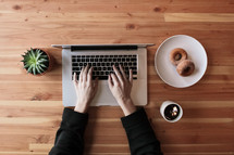 a woman typing on a laptop and donuts and coffee 