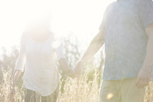 a couple walking holding hands through tall grasses 