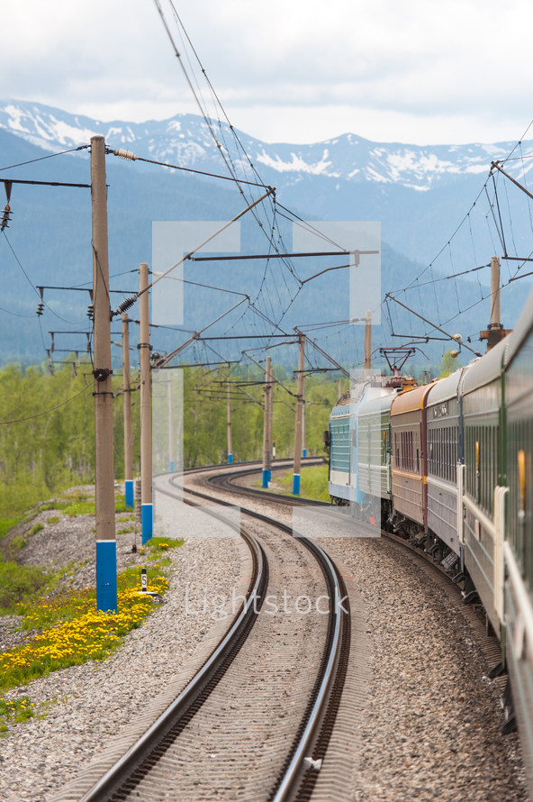 Power lines near a train on railroad tracks near a mountain range.